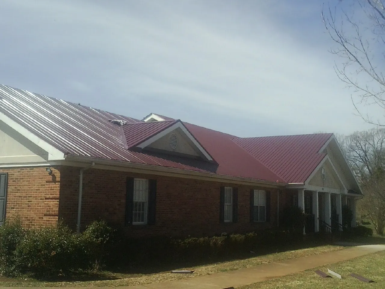 Red metal roof with gabled entries on a long brick building, from a Hail Damage Roof Repair job in Yuba City