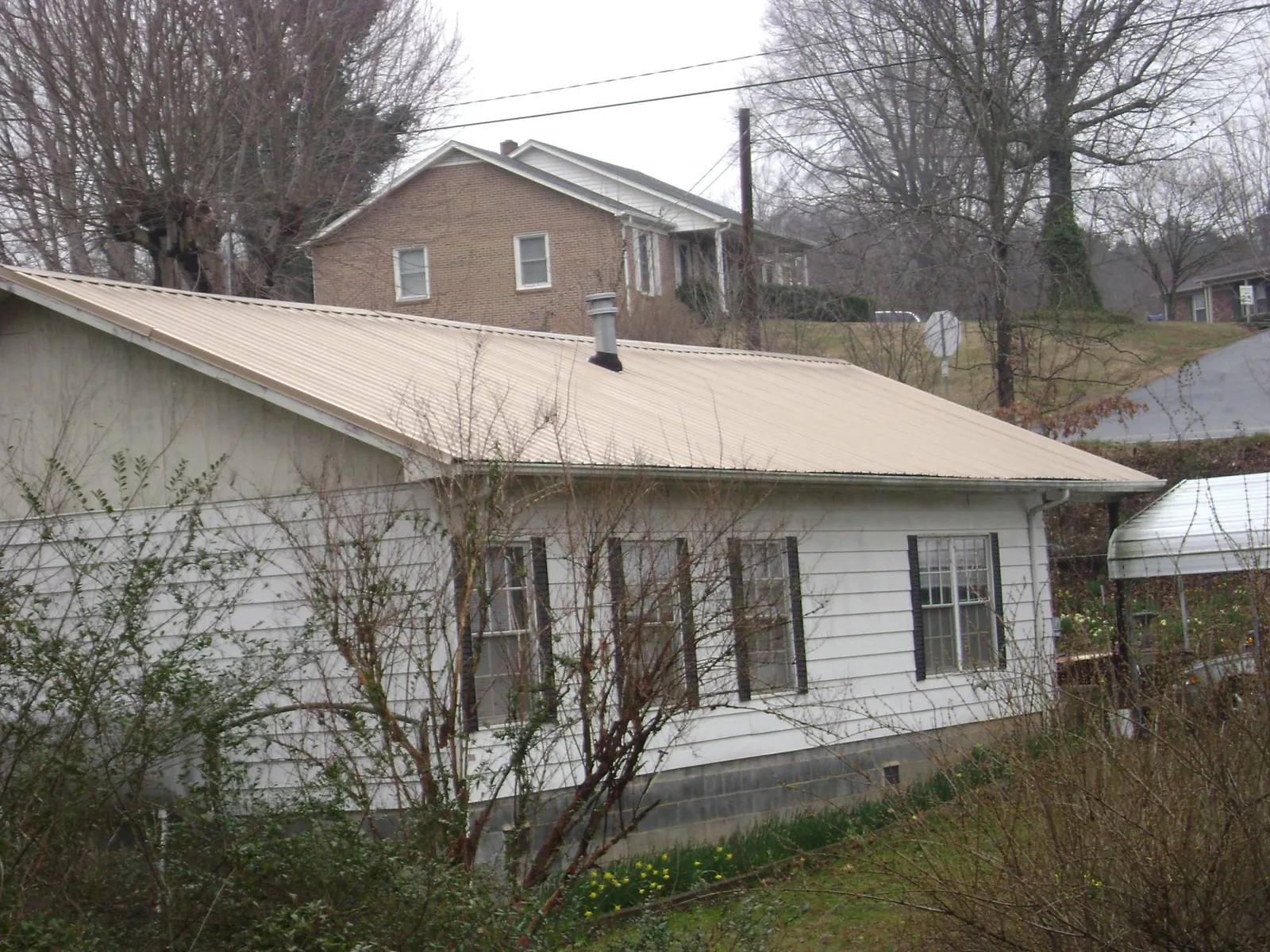 Tan metal roof on a white sided house set into a hillside — Commercial Roofing by Roofing Brothers in Yuba City